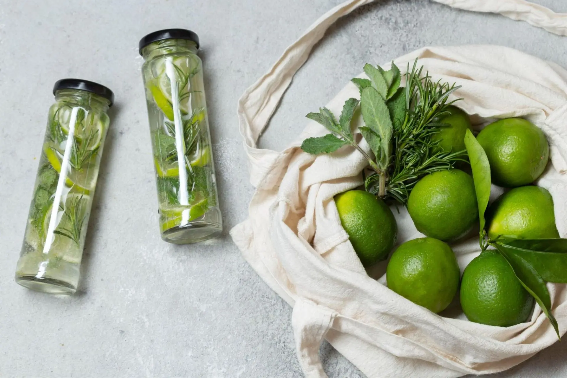Lime water in a sustainable glass bottle next to fresh limes in a basket.