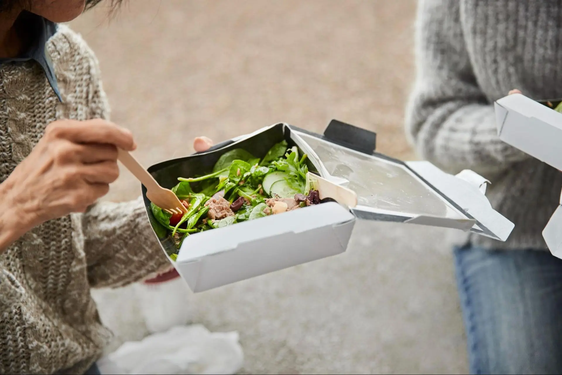 Friends eating a salad in eco-friendly paper packaging.